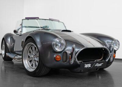 Eine graue Dax Cobra replik 427 SC mit hellgrauen Rallystreifen auf der Haube.